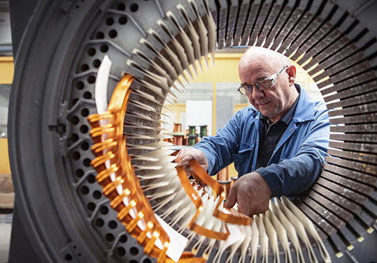 Electrical engineer installing copper windings into generator stator in electrical engineering factory